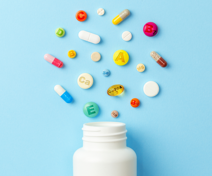 A pill bottle spilled on a blue background showing many types of vitamins and supplement capsules and tablets.